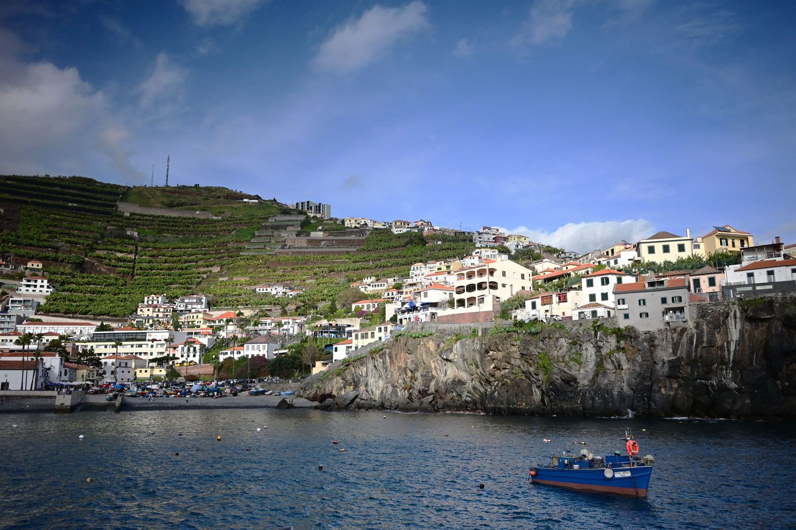 White houses on Madeira sea cliffs above a small harbor and fishing boat